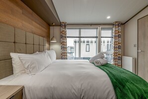 Une chambre d’hôtel avec un grand lit, une tête de lit en bois, un plaid vert et une vue sur les immeubles par la fenêtre.