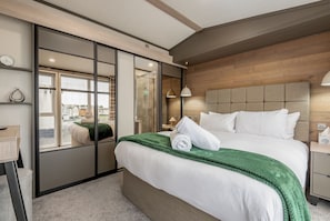 A modern hotel room with a large bed, a green throw blanket, and a wooden headboard. - Lodge No 74 | Stewart's Resort Cameron (Cameron)