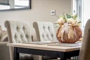 Une table à manger sur laquelle repose un panier tressé contenant un arrangement floral, le tout placé entre deux fauteuils rembourrés dont les dossiers sont capitonnés.