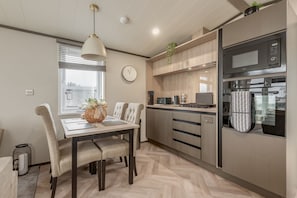 A modern kitchen with a dining area, featuring a wooden herringbone floor, built-in appliances, and a large window with blinds. - Lodge No 74 | Stewart's Resort Cameron (Cameron)