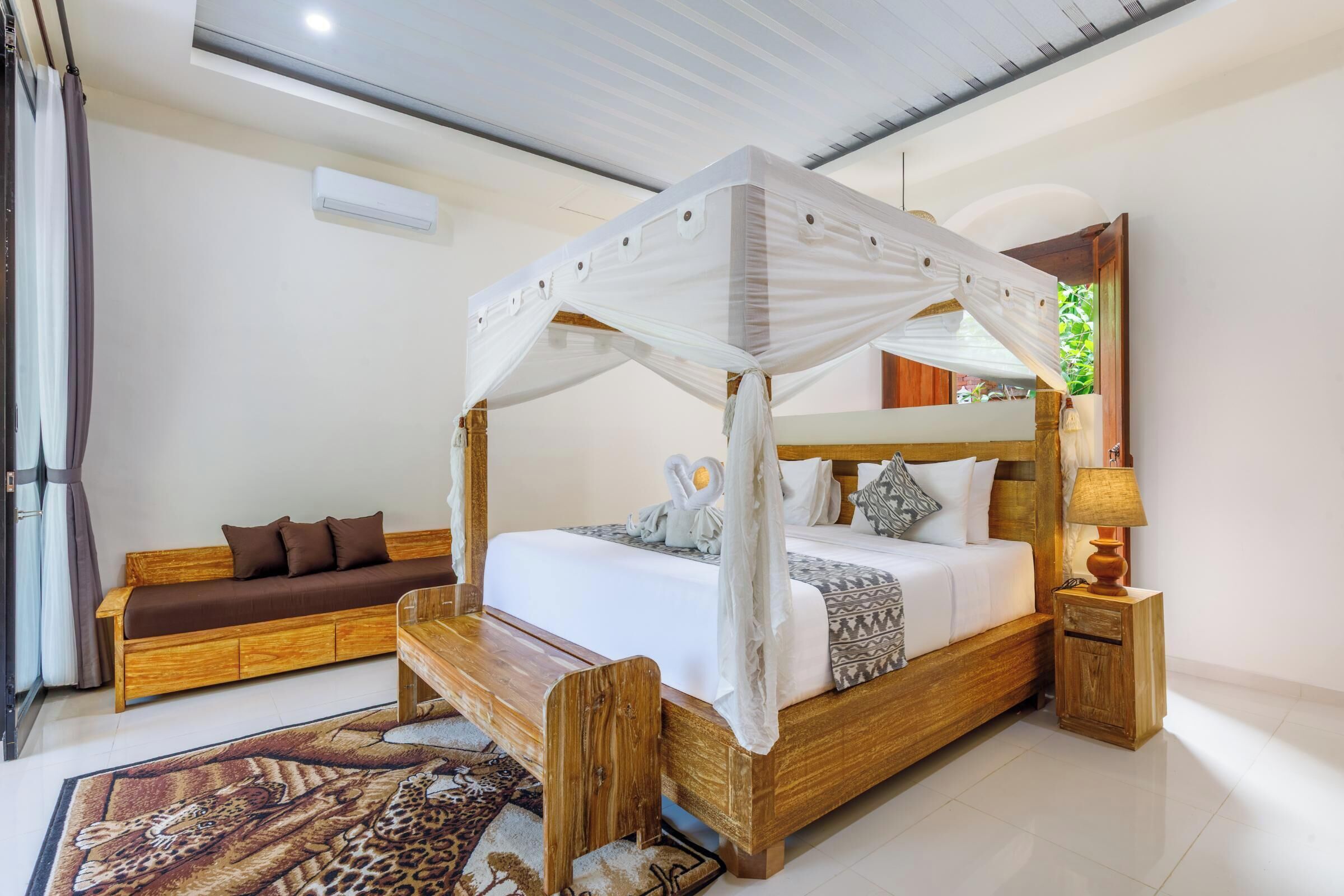 Una cama con dosel, un banco de madera, un sofá y una mesita de noche con una lámpara.