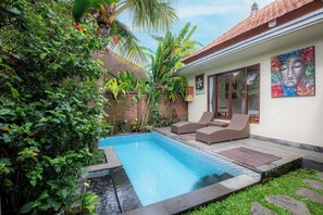 A swimming pool with lounge chairs, surrounded by lush greenery and a tiled roof.