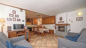 A living room with a TV, sofa, and fireplace. There is a dining area with a table and chairs. - Maison Chatelard (La Salle)