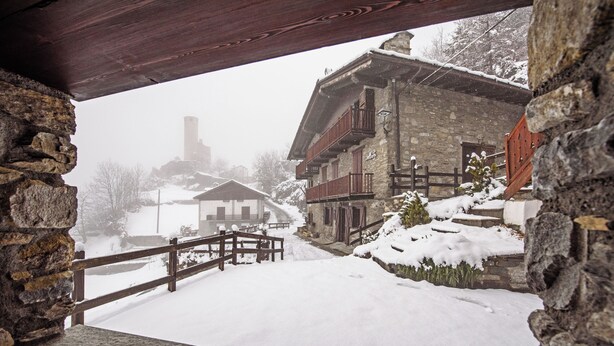 A stone building with a wooden balcony, a wooden fence, and snow-covered ground. - Maison Chatelard (La Salle)