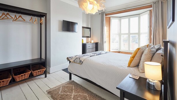 A bedroom with a bed, bedside lamp, window, and a wardrobe with hangers and baskets. - Host Stay Park Terrace (Whitby)
