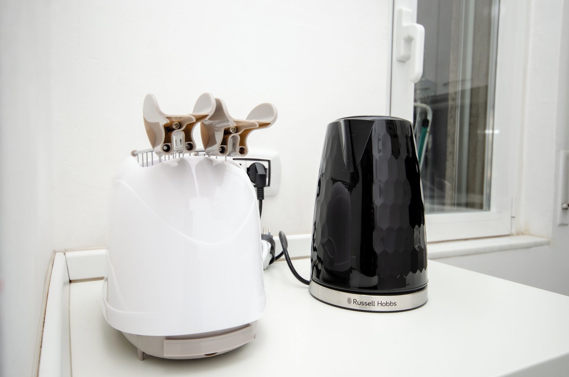 Een wit apparaat, mogelijk een koffiezetapparaat, en een zwarte container, mogelijk een koffiekan, op een witte aanrecht.