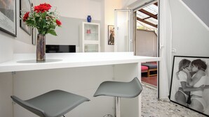 A modern kitchen with a white countertop, two grey bar stools, and a vase with red flowers. - VivimiHome - Zanella House (Milan)
