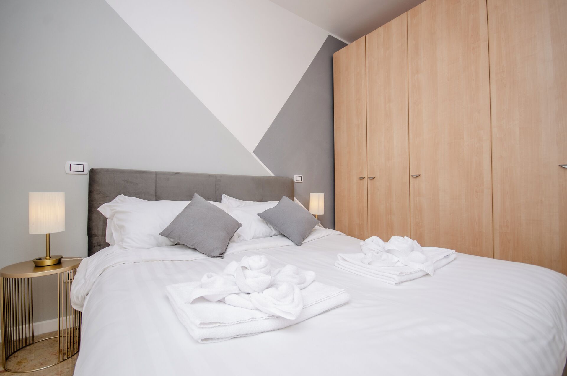 Un letto rifatto con cuscini e asciugamani, una lampada da comodino e un armadio in legno.