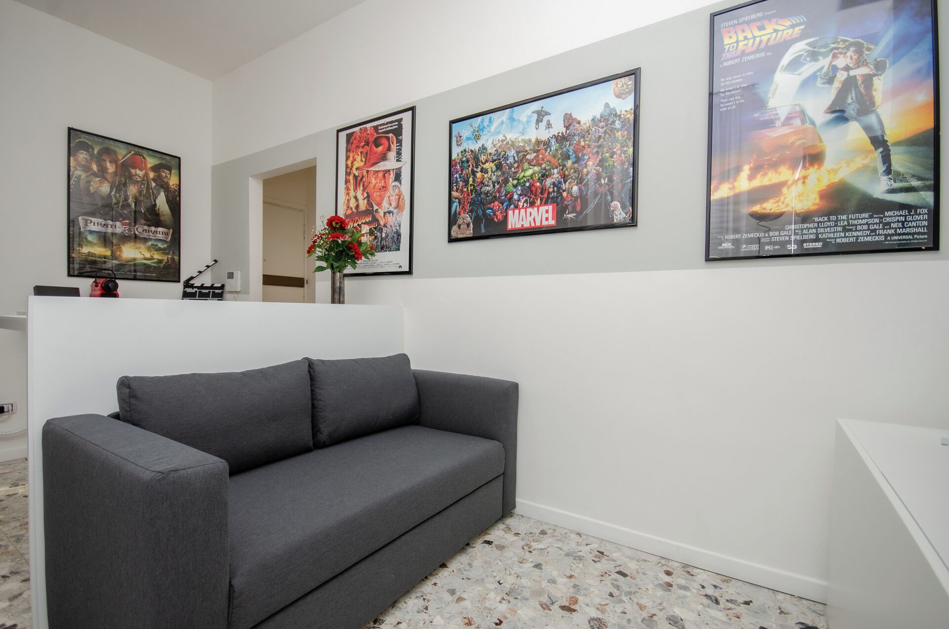 A modern living room with a grey sofa, a coffee table, and a TV. There are posters on the wall, including a Marvel poster and a movie poster.