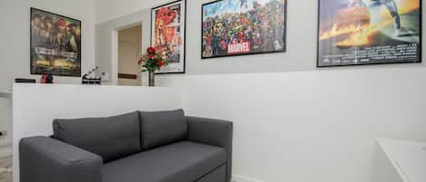 A modern living room with a grey sofa, a coffee table, and a TV. There are posters on the wall, including a Marvel poster and a movie poster.
