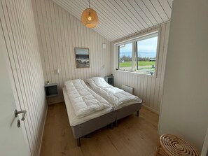A bedroom with two beds, a window with a view, a wall-mounted light, and a small bedside table. - Charming home in Marielyst - Bøtø (Væggerløse)