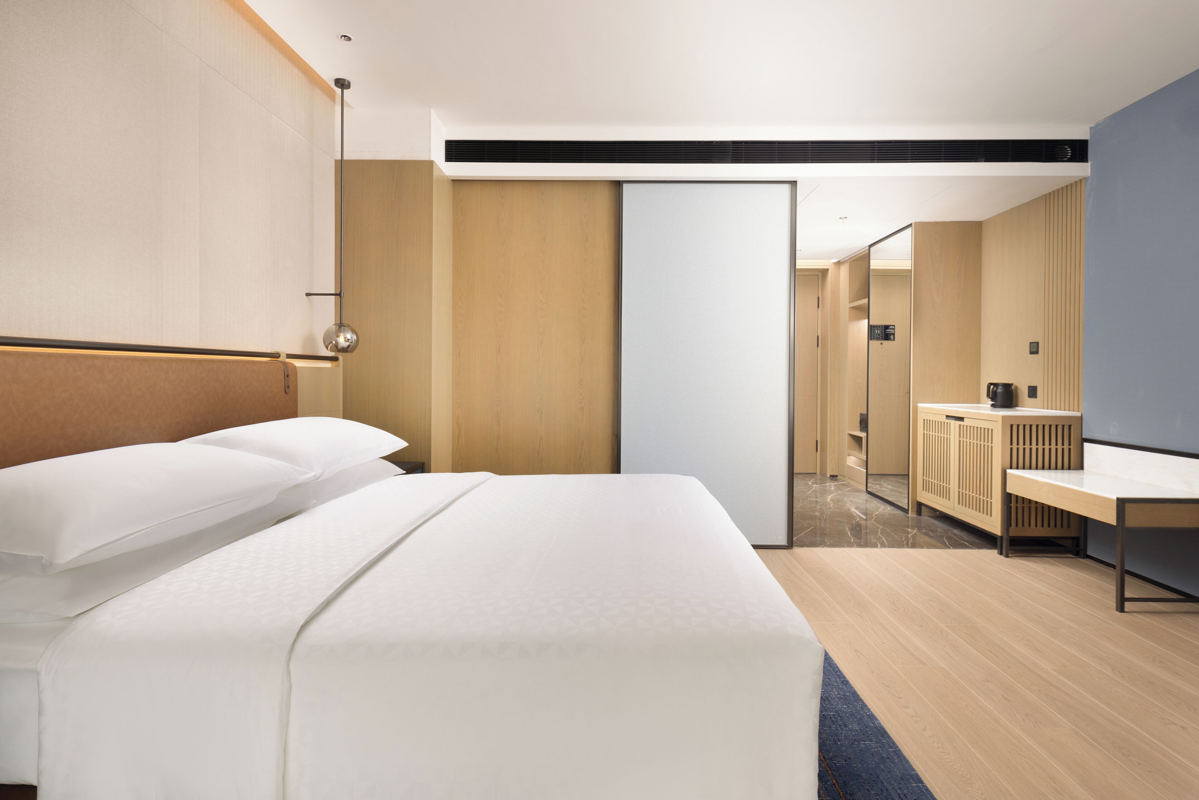 A modern hotel room with a large bed, a desk, and a mirror.