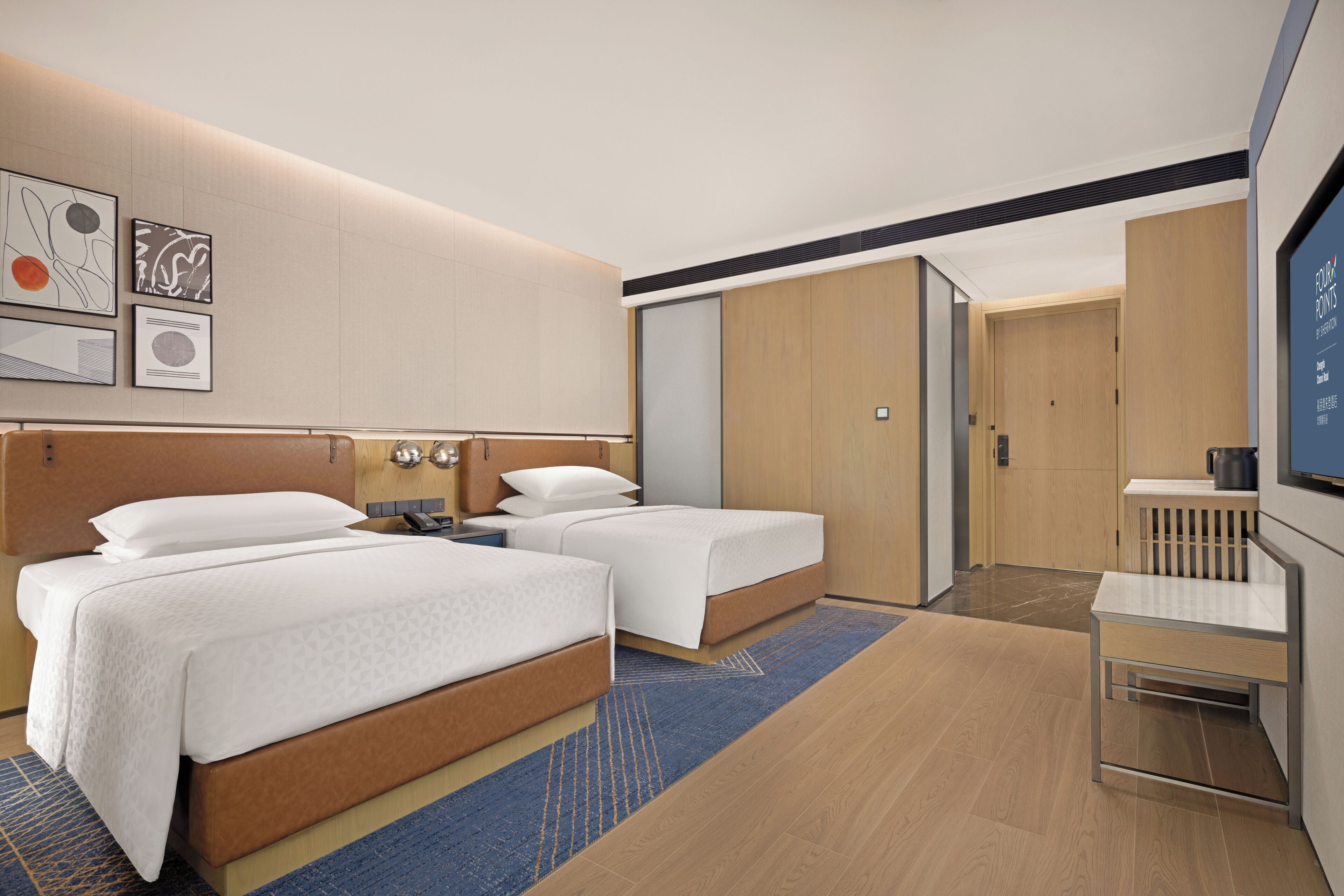Ein modernes Hotelzimmer mit zwei Betten, einem Schreibtisch, einem Fernseher und Kunstwerken an der Wand.