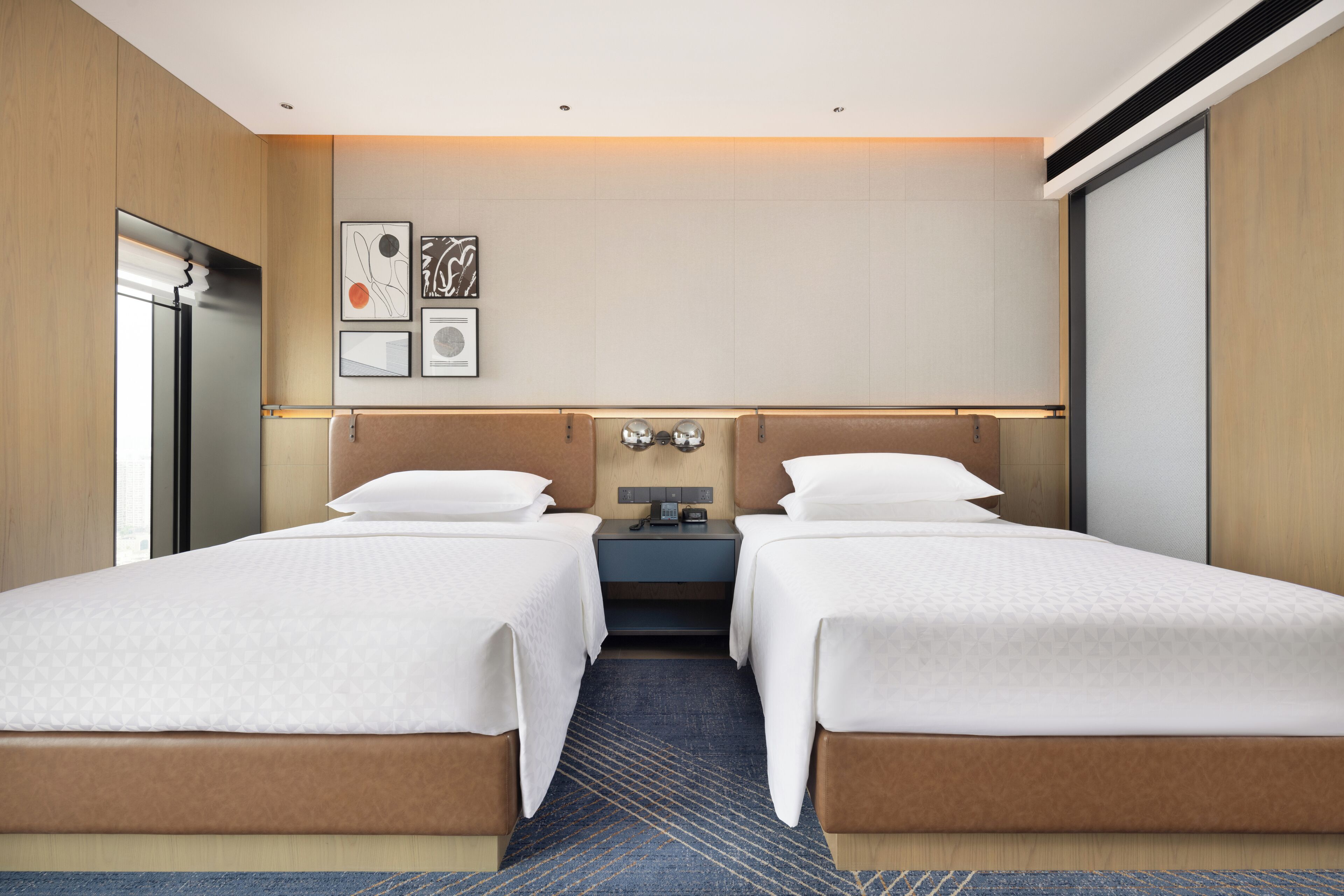 A hotel room with two beds, a nightstand, a wall-mounted TV, and artwork.