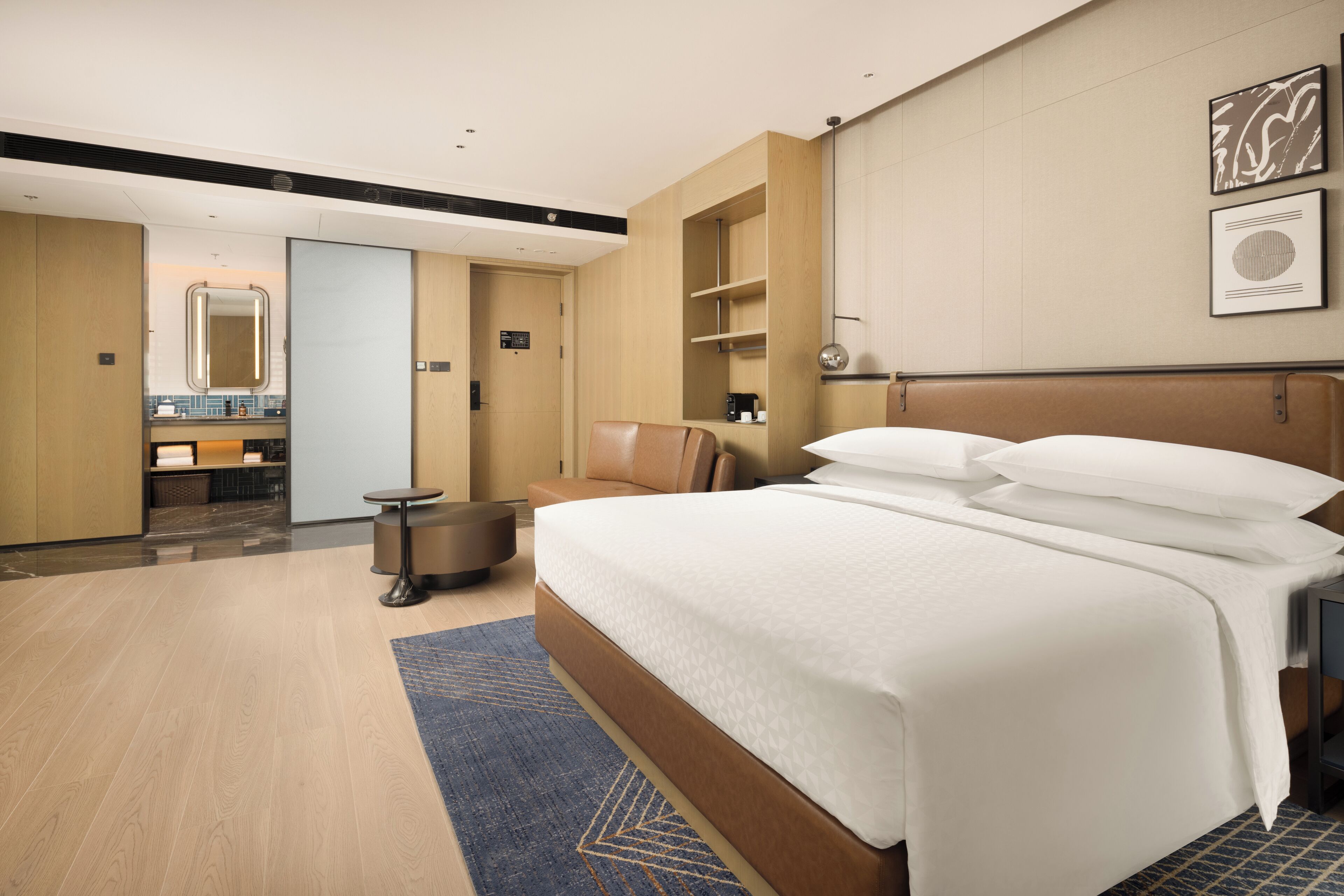 Una habitación de hotel moderna con una cama grande, una zona de estar, una pequeña mesa y un baño visible a través de una puerta abierta.