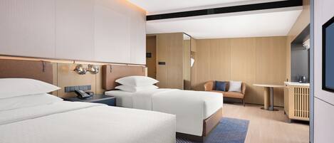 A modern hotel room with two beds, a small seating area, and a TV.