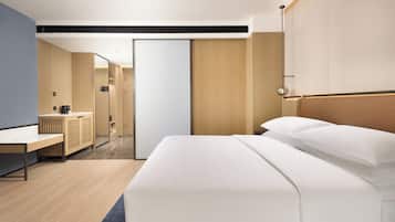 A modern hotel room with a large bed, a desk, and a wardrobe.