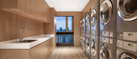 A laundry room with a sink, multiple washing machines, and a view of a cityscape through a window.