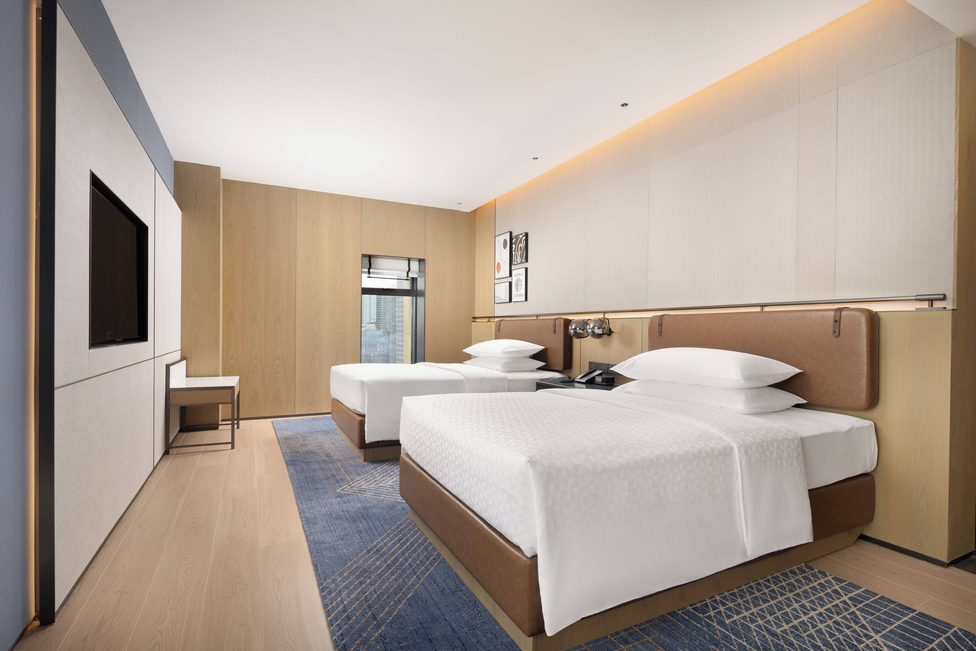Moderni hotellihuone, jossa on kaksi sänkyä, työpöytä, suuri ikkuna ja näkymä kaupunkiin.