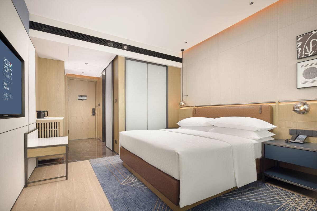 A hotel room with a bed, bedside table, and a desk with a chair.