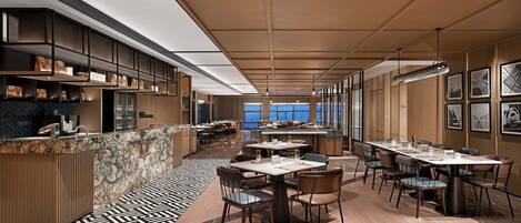 A modern dining area with a long counter, multiple tables, and chairs. There are shelves with items on the left, and a patterned floor.