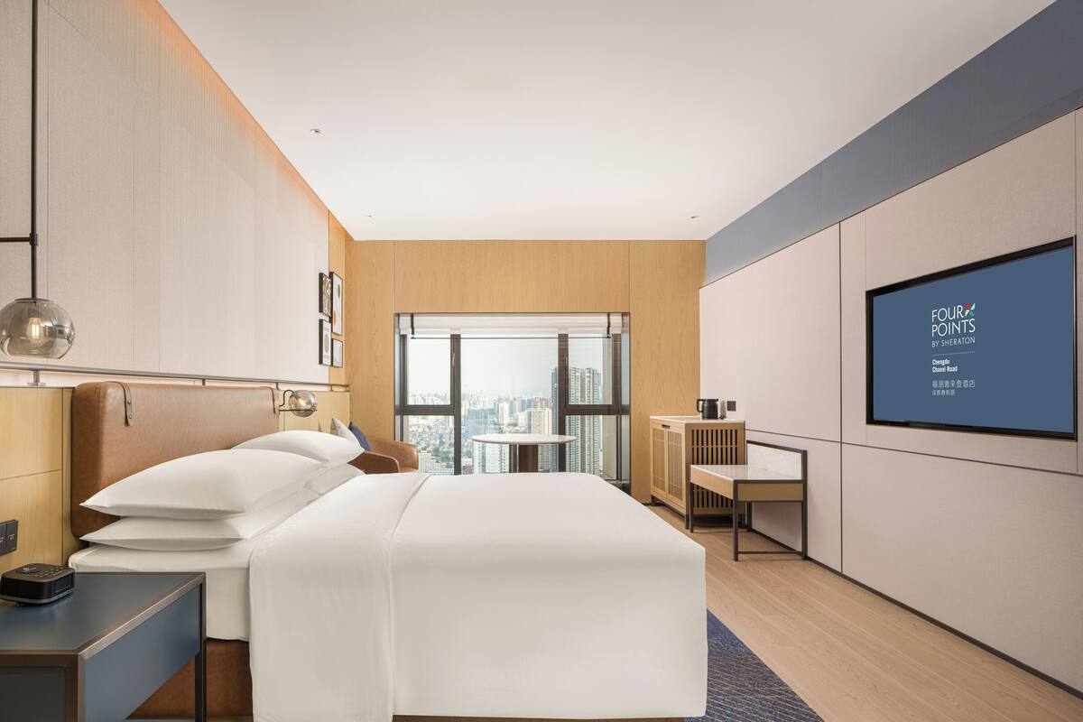 A modern hotel room with a large bed, a desk, and a city view.