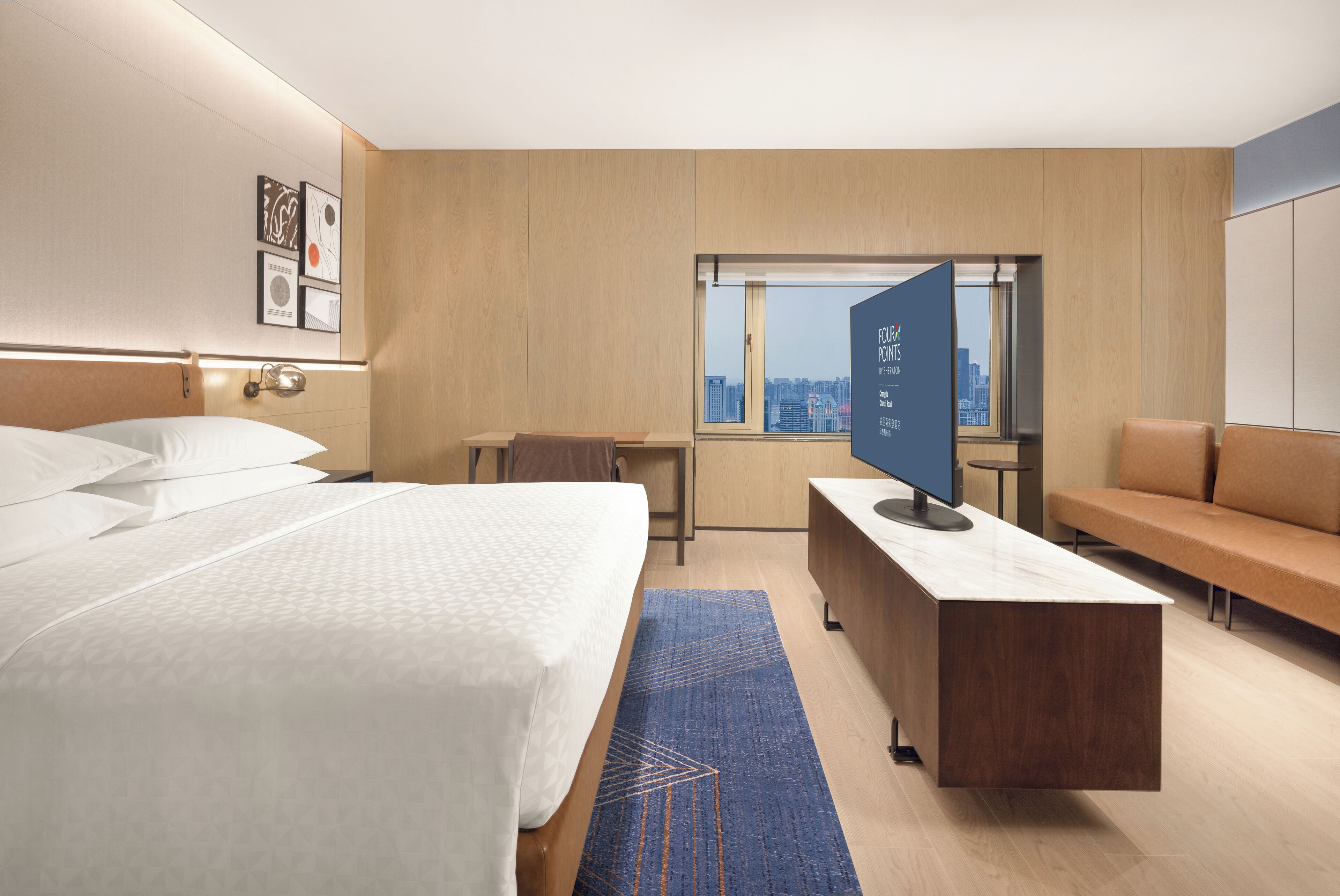 A modern hotel room with a large bed, a desk, a sofa, and a city view through the window.