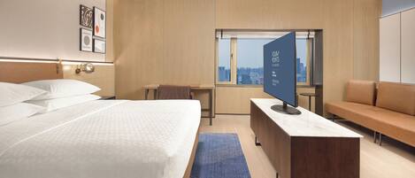 A modern hotel room with a large bed, a desk, a sofa, and a city view through the window.