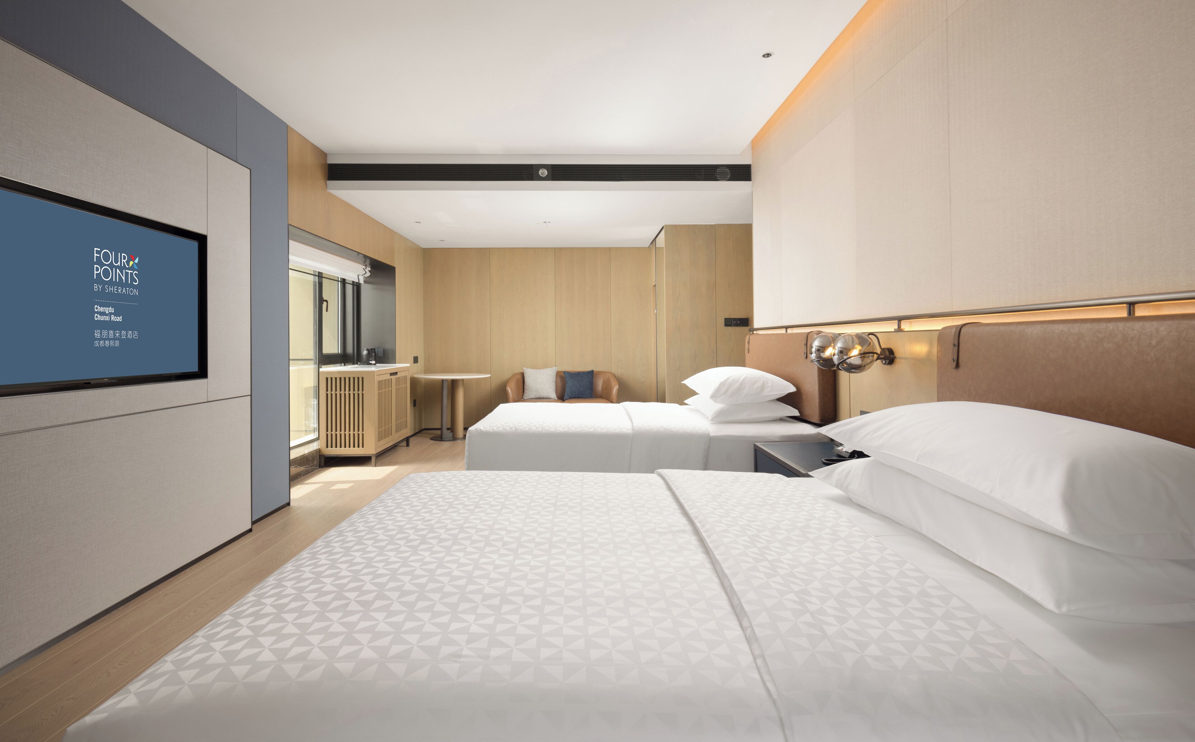 A modern hotel room with two beds, a TV on the wall, and a small table.