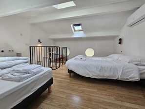 A modern bedroom with two beds, a skylight, and a circular window.
