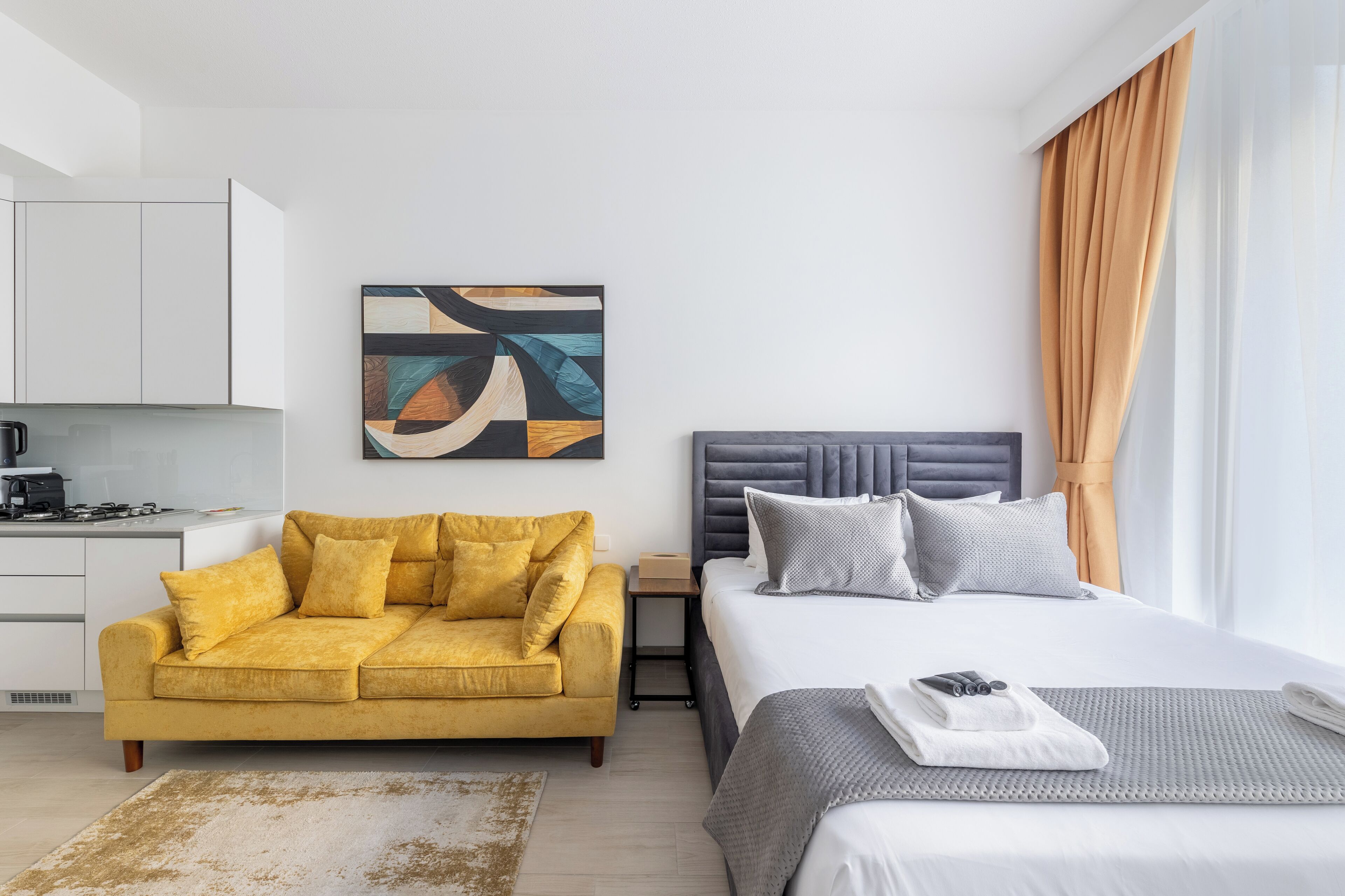 Moderni hotellihuone, jossa on sänky, sohva, työpöytä ja taulu seinällä.