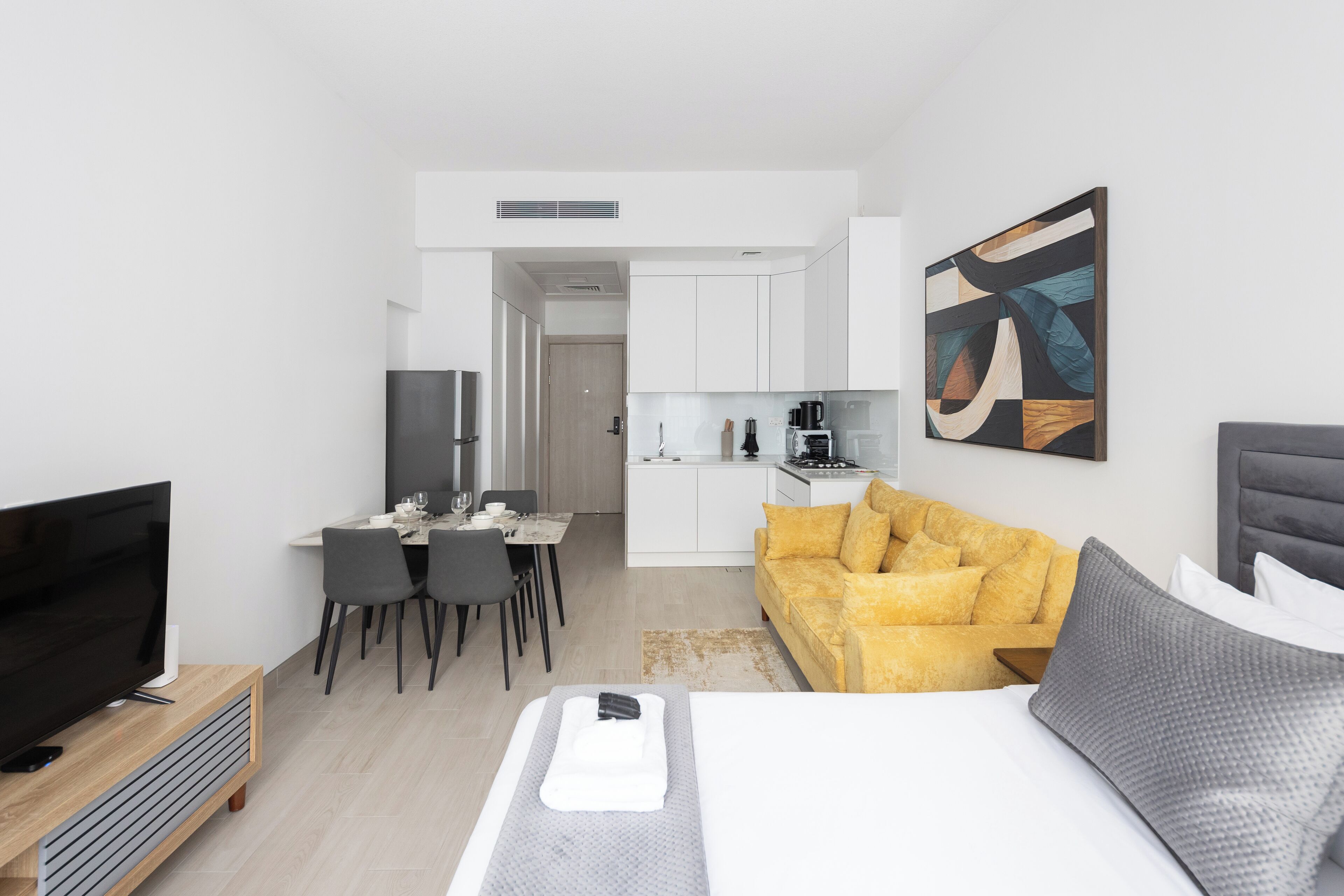 A modern hotel room with a flat-screen TV, a sofa, a dining area, and a kitchen.