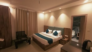 A modern hotel room with a large bed, a bedside table, a chair, and a bathroom visible through an open door.