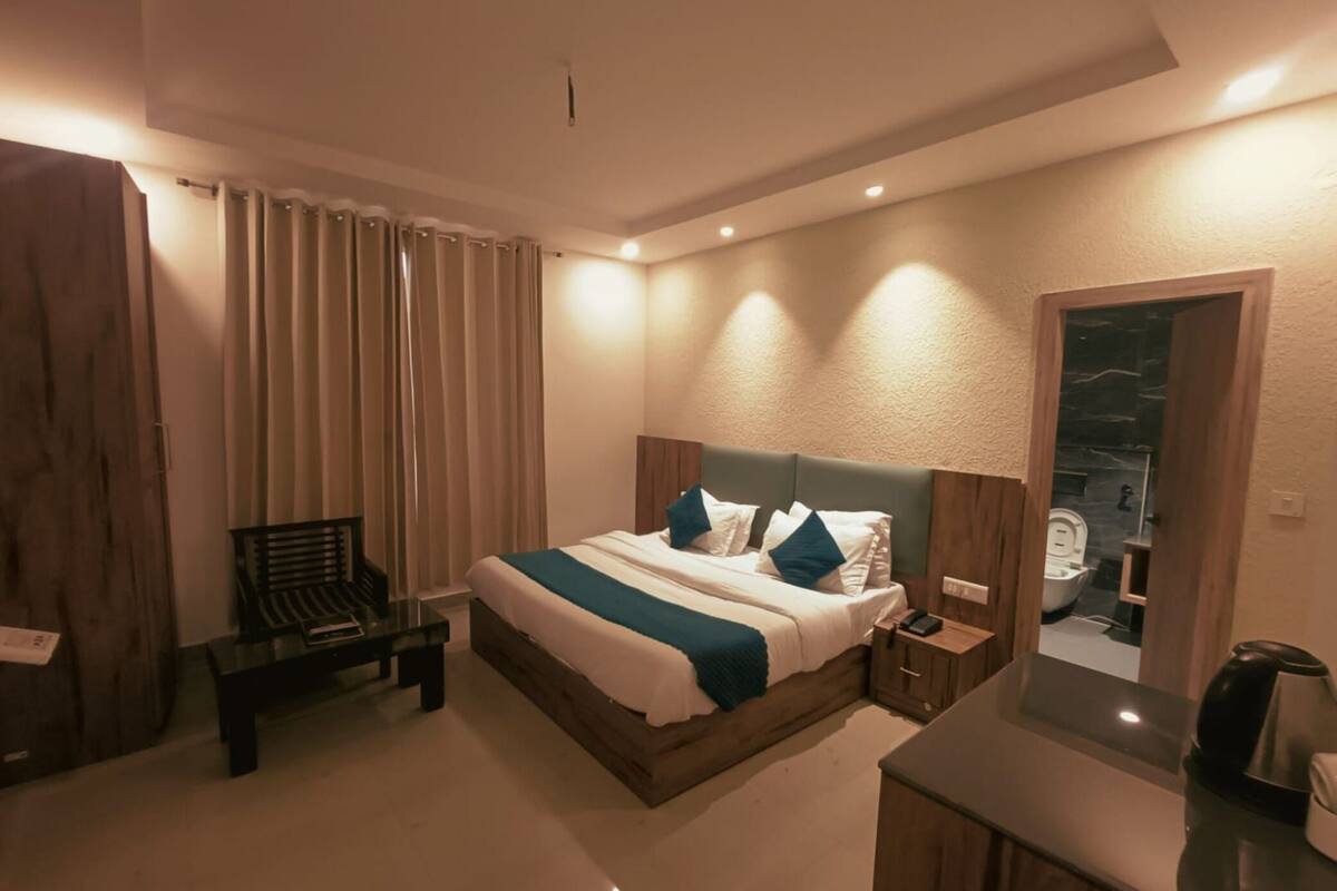 A modern hotel room with a large bed, a bedside table, a chair, and a bathroom visible through an open door.