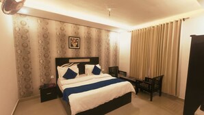 A hotel room with a bed, a chair, a desk, a fan, and curtains.