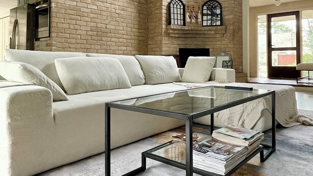 A spacious living room with a brick fireplace, a glass coffee table, and a modern ceiling fan.