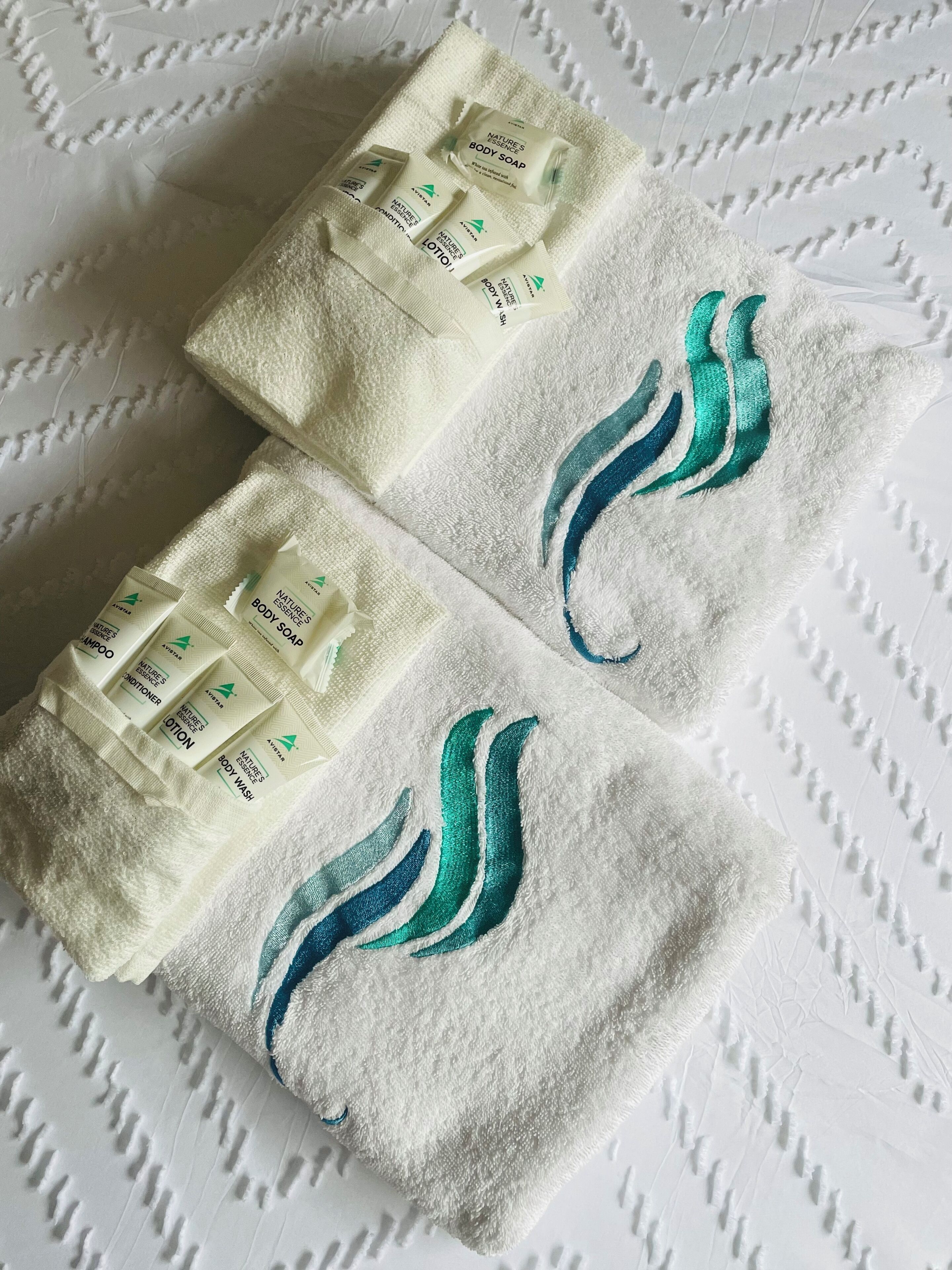 Two towels with embroidered designs and toiletries on a textured white surface.