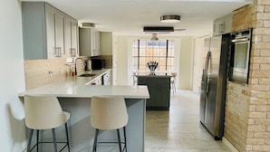 A modern kitchen with a central island, bar stools, a refrigerator, and a brick accent wall.