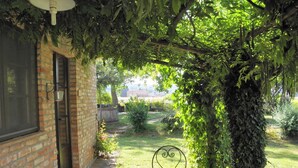 A patio area with a tiled table and a metal chair, surrounded by lush greenery and a brick wall. - La Vecchia Cedraia Apartment, Wifi, Perugia (Santa Maria)