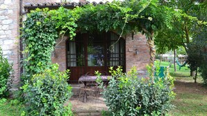 Un bâtiment en briques avec une porte en bois, une petite table et quelques chaises à l’extérieur.