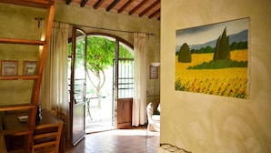 A room with a wooden ceiling, a dining table with chairs, a large window with curtains, and a painting of a field on the wall.