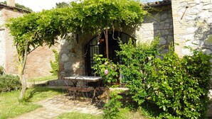 A stone building with a garden patio featuring a table and chairs, surrounded by lush greenery and a stone wall.