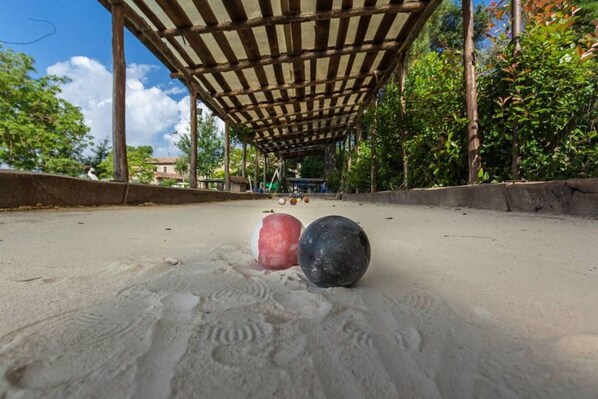 Una cancha de arena con dos pelotas, una pérgola de madera sobre ella y árboles al fondo.