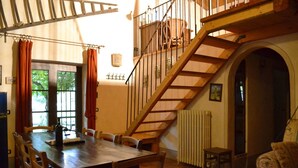Ein Essbereich mit Holztisch und -stühlen, eine Treppe mit hölzernem Geländer und ein Heizkörper an der Wand.