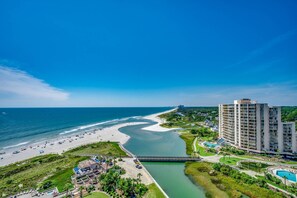 Un complejo turístico frente al mar, con playa, canal navegable, piscina y un hotel de gran altura.