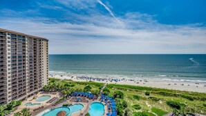 A hotel with a large pool area, a beach, and a view of the ocean.