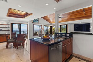A modern kitchen with a central island, wooden ceiling, and large windows offering ocean views. - Wailea Elua 1304 - Spectacular Oceanfront Condo with Panoramic Views (Wailea, Maui)