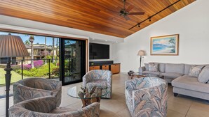 A modern living room with a wooden ceiling, a large TV, and a sofa. - Wailea Elua 1304 - Spectacular Oceanfront Condo with Panoramic Views (Wailea, Maui)