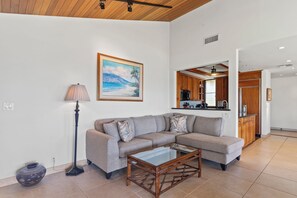 A living room with a sectional sofa, a glass coffee table, a lamp, and a painting of a beach scene.