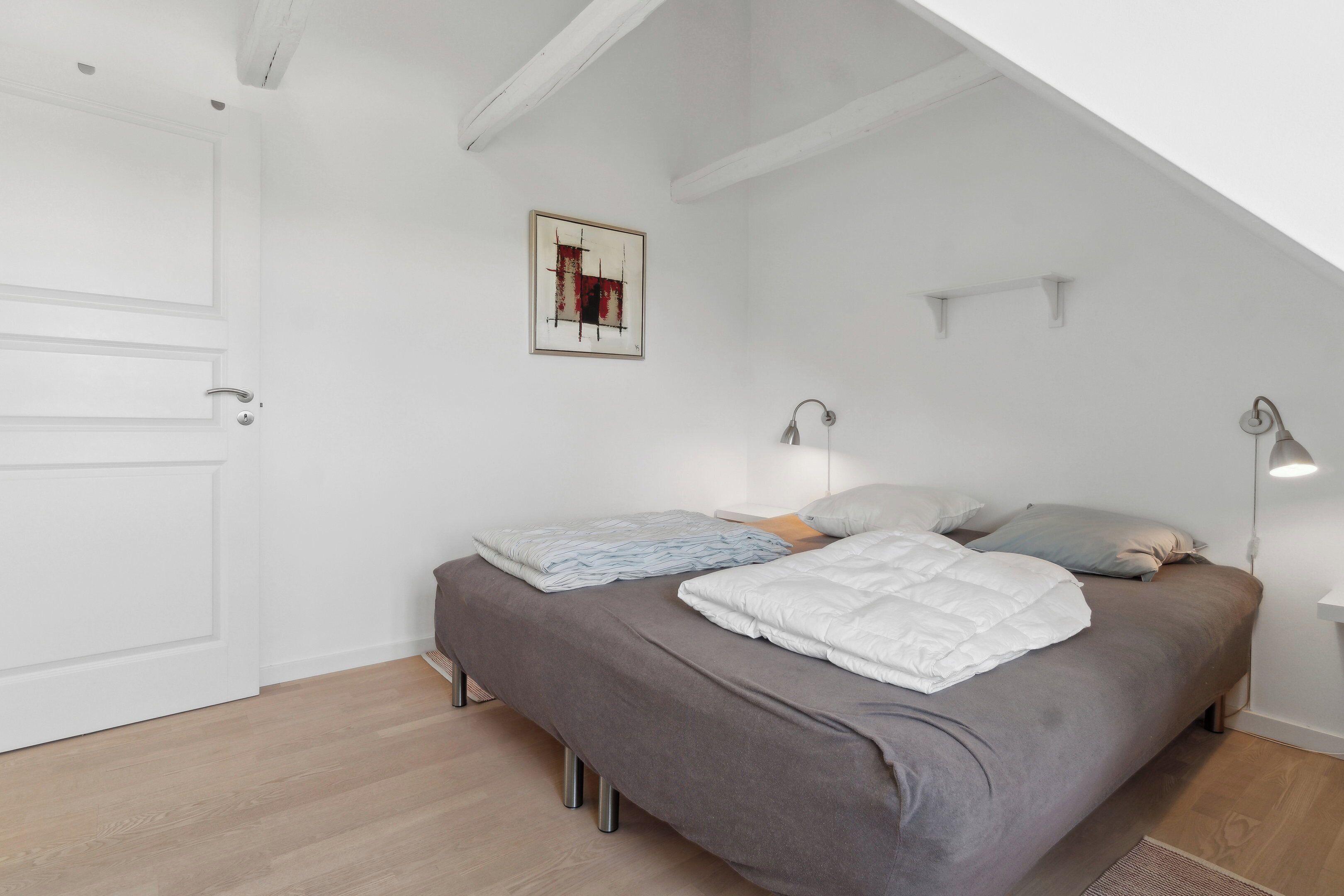Ein Schlafzimmer mit einem Bett, zwei Nachttischlampen, einem gerahmten Bild an der Wand und einer weißen Tür.